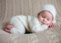 Beatiful baby boy in white knitted cloths and hat, sleeping sweetly posed in bed